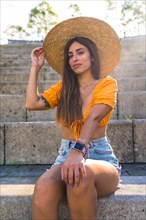 Lifestyle of a young caucasian brunette walking in the summer in a park in the city. Portrait of the girl with a hat at sunset