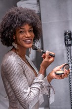 A young black girl with afro hair putting on makeup before the party with a smile. Exclusive party