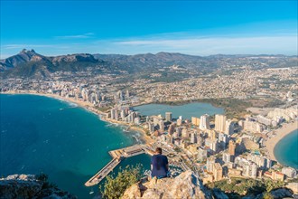 A young man sitting on top of the Penon de Ifach Natural Park in Calpe