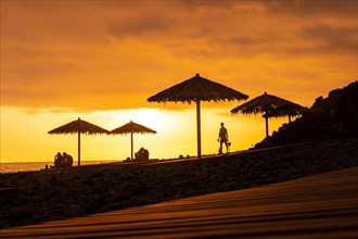 Orange sunset on the umbrellas at Ponta do Sol beach