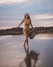 A brunette woman having fun with a swimsuit and a pareo walking along the beach in summer at sunset