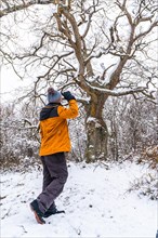 A young woman in a yellow jacket under a beautiful giant tree frozen by the winter cold. Snow in the town of Opakua near Vitoria in Araba
