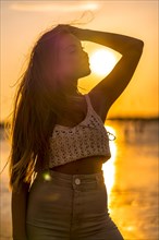 Summer lifestyle. A young blonde Caucasian woman in a white short wool sweater on a beach sunset. Thinking and looking at the sea