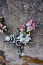 Artificial roses behind a cross on a weathered wall on a grave in a cemetery