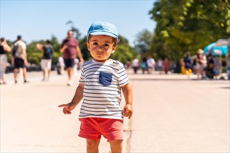 Portrait of a one year old Caucasian boy looking at the camera walking in a park with a cap