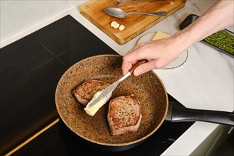 Unrecognizable man adding butter to frying pan with beef steaks