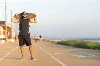 A man standing on the bike path holding a skateboard on his shoulders. Mid shot