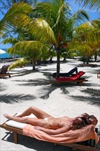 Woman sunbathing topless on sun lounger beach lounger under coconut palms