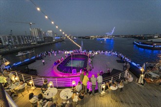 Passengers sit on the Lido Deck of the cruise ship Vasco da Gama and watch the Blue Port light art event in the harbour