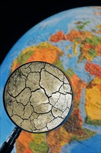 Cracked earth by drought seen through magnifying glass held against illuminated terrestrial globe