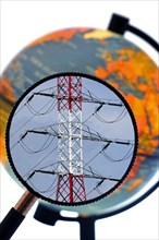 High voltage pylon in red and white through magnifying glass held against illuminated terrestrial globe
