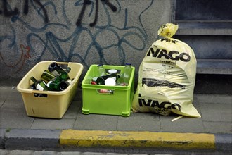 Plastic containers with glass bottles and garbage bag with household waste in front of house in city street