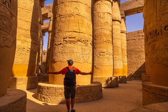 A young tourist walking among the columns with hieroglyphs inside the Karnak Temple
