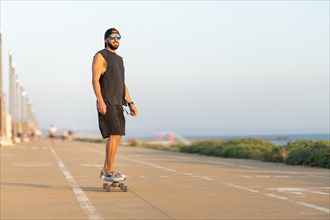 A cool guy riding a skateboard on the road by the ocean. Mid shot