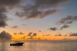 Small motorboat anchored in calm sea in safe bay during sunset with coloured sky and clouds