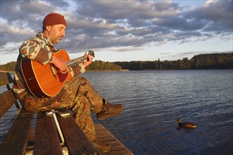 Man playing guitar on a jetty by the lake