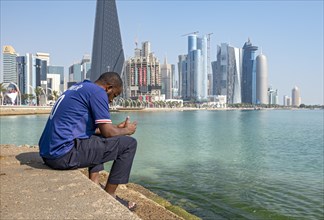 Man sits on steps of Corniche with skyscrapers in background