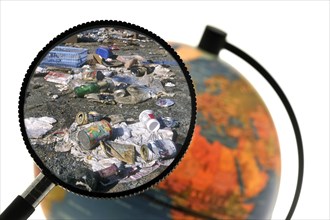 Rubbish at refuse dump seen through magnifying glass held against illuminated terrestrial globe