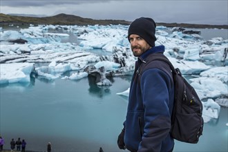 A young man with a backpack looking at the Jokulsarlon Ice Lake in the golden circle of southern Iceland