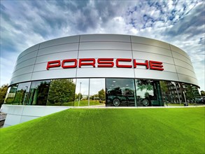 View of futuristic looking building with typical reduced architecture of showroom sales house of car brand car manufacturer Porsche with lettering Porsche at representation of car dealer Gottfried Sch...