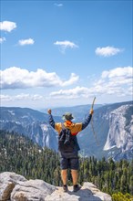A young man with a walking stick and arms raised at Sentinel Dome in Yosemite National Park. United States