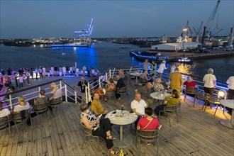 Passengers sit on the Lido Deck of the cruise ship Vasco da Gama and watch the Blue Port light art event in the Port of Hamburg in the evening