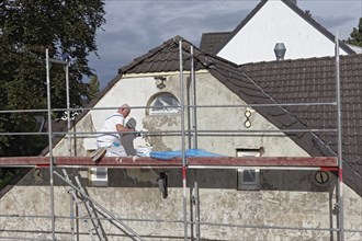 Painter on scaffolding plastering the facade of a house from 1830