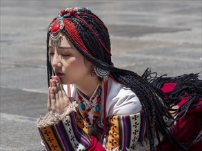 Tibetan young woman with festive hair ornaments and necklaces praying on the floor