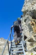 Hikers climb metal stairs up a rock face to the Konkordiahuette mountain hut