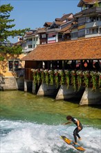 Surfer Surfing on River Aare in City of Thun from Untere Schleuse Bridge in a Sunny Summer Day