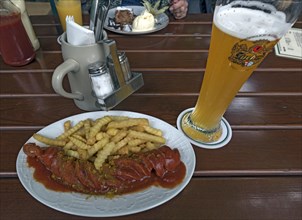 Curry sausage and chips and wheat beer on a table in a garden pub