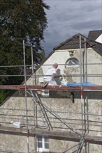 Painter on scaffolding plastering the facade of a house from 1830