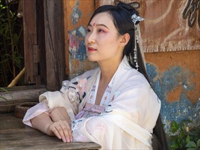 Woman in Chinese nostalgia with old luxurious white dress in front of old house