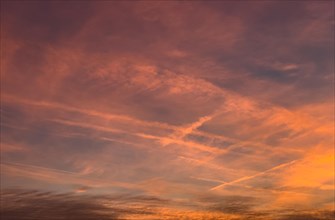 Coloured reddish orange sky Evening sky at dusk with veiling clouds Cirrostratus and contrails from air traffic Passenger aircraft