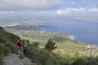 Hikers on the peninsula of La Victoria and view of the bay of Pollenca