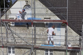 Painters on scaffolding plastering the facade of a house from 1830