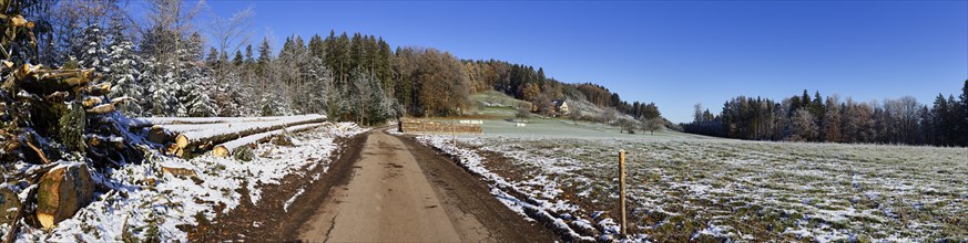 Slightly snowy landscape in the Black Forest with small road and wood pile near Hofstetten