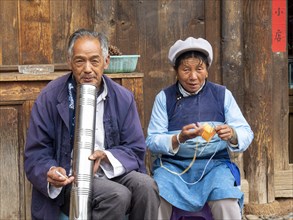 Old Chinese couple sitting in front of wooden house