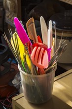Plastic conatiner filled with colourful utensils for sale inside second hand goods and chattels store