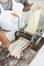 Close up baker cutting raw dough into tagliatelle pasta machine