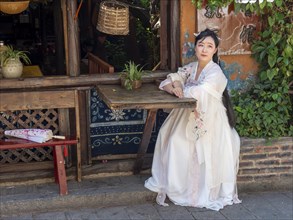 Woman in Chinese nostalgia with old luxurious white dress in front of old house