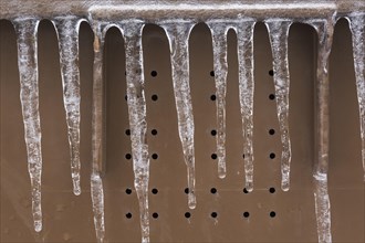 Close-up of icicles against a brown perforated background