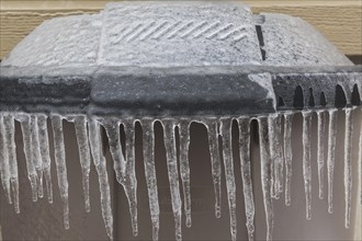 Brown and black plastic trash can covered with ice and icicles