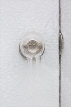 Close-up of ice covered doorknob with keyhole and strike plate on white door