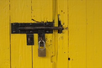 Yellow painted wood plank barn door locked with brass padlock