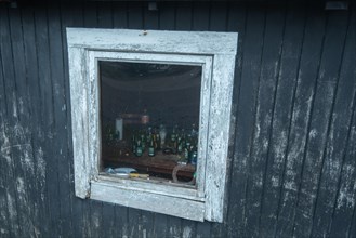 Beer bottles and cigarette packets behind the window of an old fishing hut