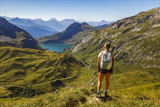 A young woman stands on a hiking trail on a mountain and looks at the Spullersee in Vorarlberg Lech Austria