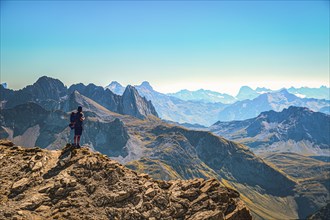 A hiker stands on the summit of the Mohnefluh in the Lechquellen mountains in Austria and looks over the Alps