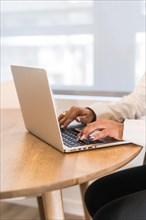 Vertical photo with close-up of a businesswoman's hands working on laptop at wooden table