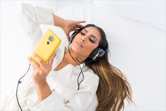 Top view of a beauty woman in comfortable clothes listening to music lying on a bedroom of an hotel